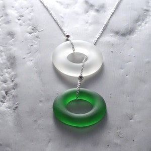 May include: A silver chain necklace with two glass rings. The top ring is white and the bottom ring is green.