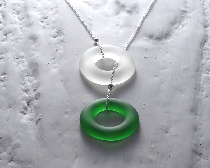 May include: A silver chain necklace with two glass rings. The top ring is white and the bottom ring is green.