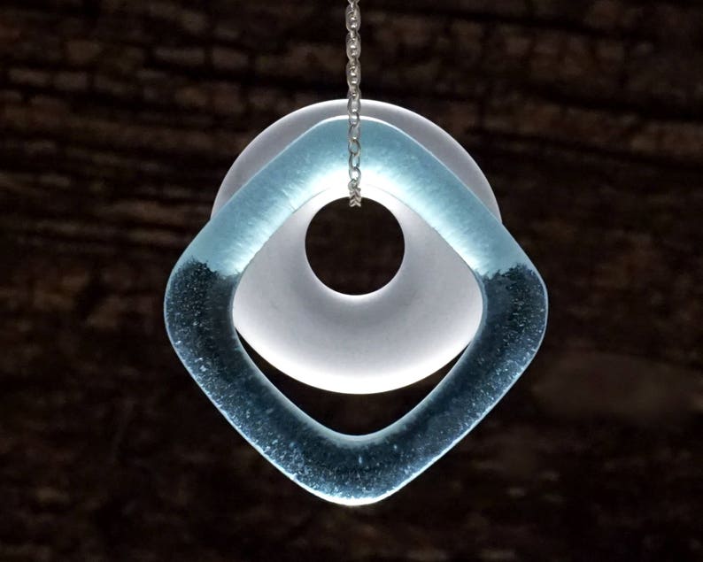 May include: A silver chain necklace with a pendant made of two overlapping glass circles. The larger circle is white and the smaller circle is light blue.