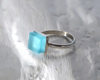 May include: A silver ring with a square, light blue gemstone.
