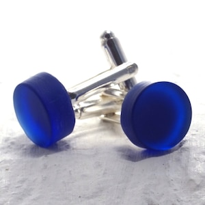 May include: A pair of cufflinks with a silver base and round, blue glass tops.
