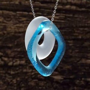 May include: A necklace with a blue and white glass pendant. The pendant is shaped like a figure eight, with the blue glass forming the outer loop and the white glass forming the inner loop.