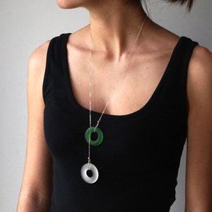 May include: A silver chain necklace with two circular pendants. The top pendant is green glass and the bottom pendant is clear glass.