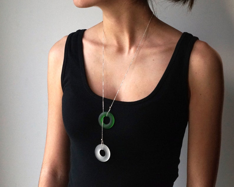 May include: A silver chain necklace with two circular pendants. The top pendant is green glass and the bottom pendant is clear glass.