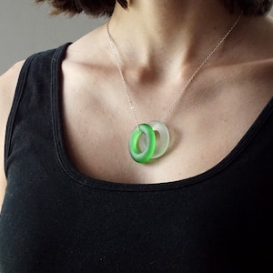 May include: A silver chain necklace with a green and clear glass pendant. The pendant is made of two overlapping circles.