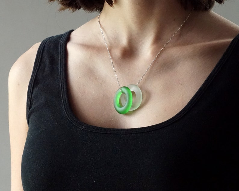 May include: A silver chain necklace with a green and clear glass pendant. The pendant is made of two overlapping circles.