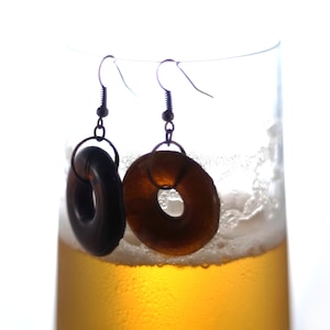 May include: A pair of earrings with dark brown wooden donut-shaped charms hanging from a glass of beer.