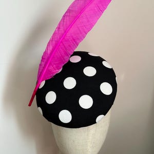 Puede incluir: Un sombrero de lunares blanco y negro con una pluma rosa brillante.