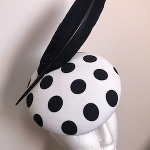 Peut inclure: Un chapeau blanc à pois noirs et une plume noire sur le dessus.