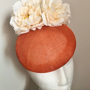 May include: A terracotta-colored hat with a wide brim and a white flower embellishment.
