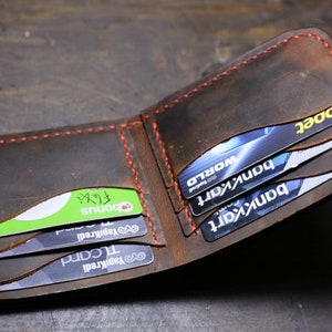 Op de afbeelding: Een bruine leren portemonnee met rode stiksels, open om meerdere creditcards en een groene kaart met het woord "Bonus" te laten zien.