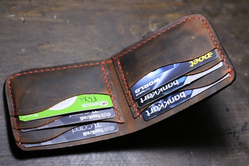 Op de afbeelding: Een bruine leren portemonnee met rode stiksels, open om meerdere creditcards en een groene kaart met het woord "Bonus" te laten zien.