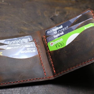 Op de afbeelding: Een bruine leren portemonnee met rode stiksels, open om meerdere kaartsleuven te laten zien. De portemonnee is gevuld met verschillende creditcards, waaronder een "bankKart"-kaart, een "Yapikredi"-kaart en een "bonus Flexi"-kaart.
