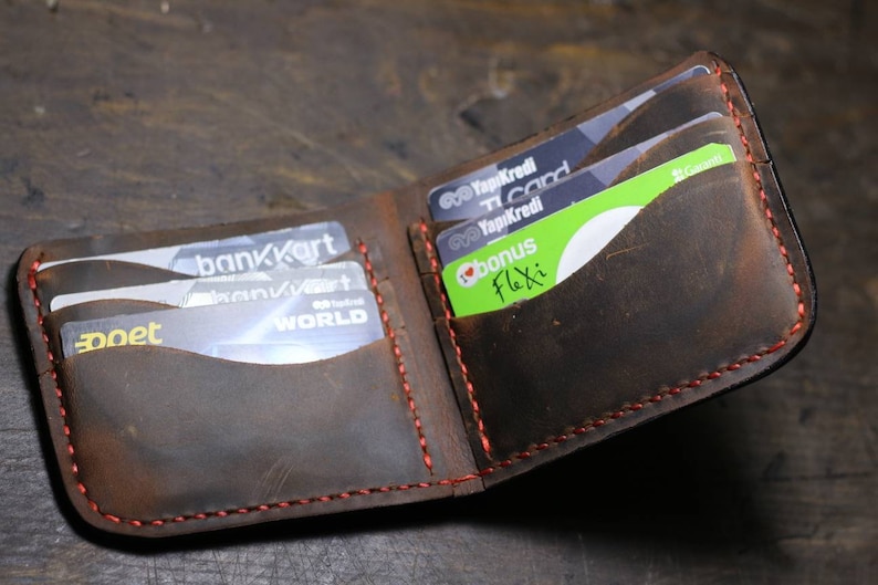 Op de afbeelding: Een bruine leren portemonnee met rode stiksels, open om meerdere kaartsleuven te laten zien. De portemonnee is gevuld met verschillende creditcards, waaronder een "bankKart"-kaart, een "Yapikredi"-kaart en een "bonus Flexi"-kaart.