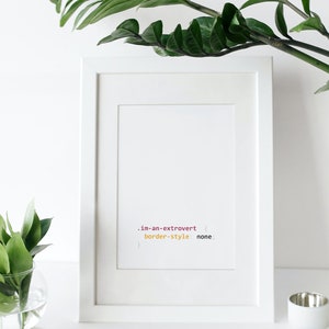 Peut inclure: Cadre blanc avec un passe-partout blanc et une impression de code qui lit '.im-an-extrovert { border-style: none; }' en texte rose, jaune et noir.