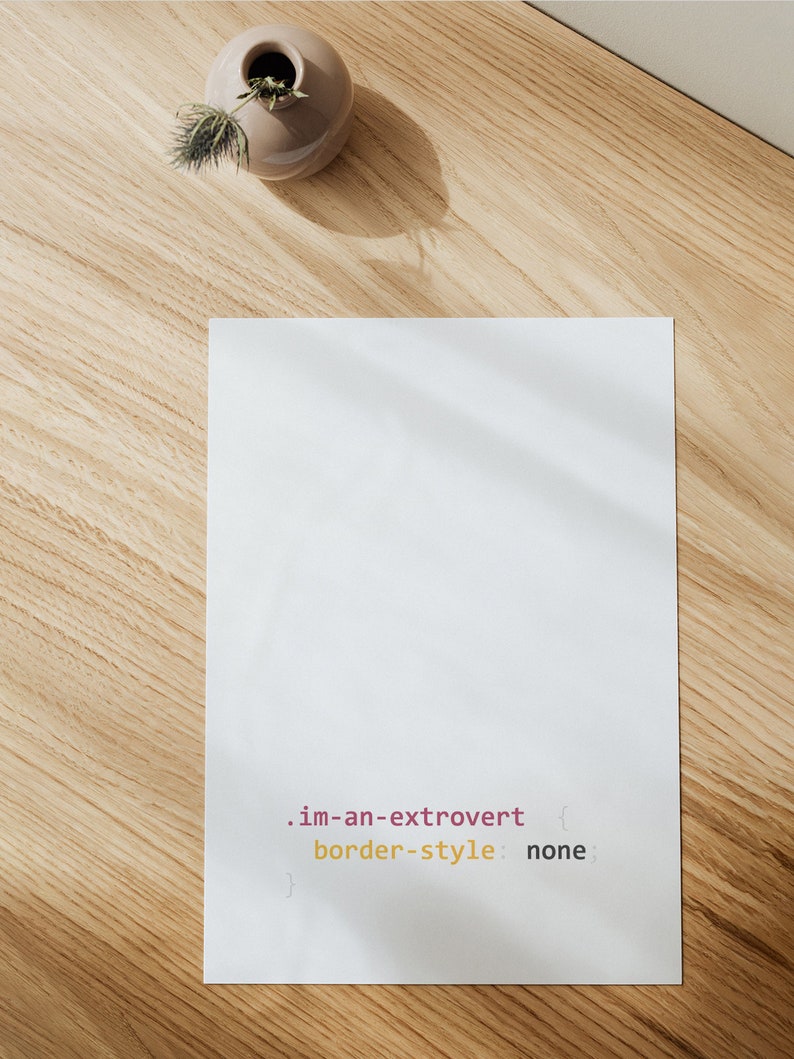 Peut inclure: Une feuille de papier blanche avec le texte ".im-an-extrovert { border-style: none }" &eacute;crit en rose et jaune sur une surface en bois.