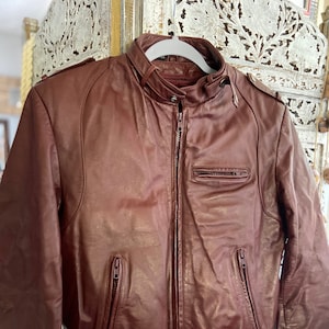 May include: A burgundy leather bomber jacket with a zipper closure and two zippered pockets. The jacket has a ribbed knit collar, cuffs, and waistband.