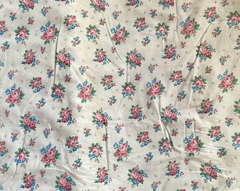 May include: White fabric with a repeating floral pattern. The pattern features clusters of pink and blue roses with green leaves, scattered across the fabric. The overall design is a classic, vintage floral print.