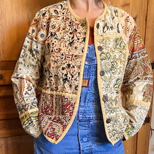 May include: A cream-colored jacket with a patchwork design featuring various floral and geometric patterns. The jacket has a button-up front and a round neckline. The jacket is made of a soft, lightweight fabric.