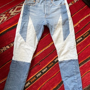 May include: Blue denim jeans with white denim panels on the sides and legs. The jeans have a straight leg fit.