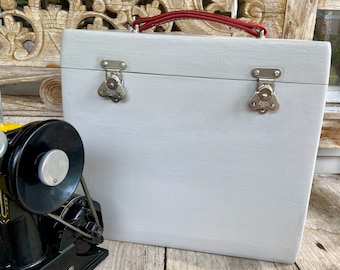 May include: A white wooden box with a red leather handle and two silver latches. The box is closed and has a smooth, painted surface.