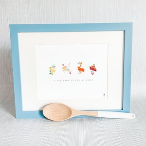 Puede incluir: Una impresi&oacute;n enmarcada con un marco azul y un fondo blanco. La impresi&oacute;n presenta cuatro rebanadas de pastel diferentes con diferentes rellenos, cada una representando una estaci&oacute;n diferente. El texto "A Pie for Every Season" est&aacute; impreso debajo de las rebanadas de pastel.