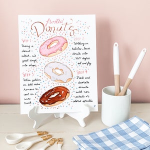 May include: A watercolor illustration of frosted donuts with sprinkles. The image includes instructions for making donuts, including using a donut cutter, frying in 365 degree oil, and frosting and decorating with sprinkles.