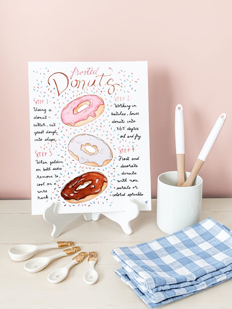 May include: A watercolor illustration of frosted donuts with sprinkles. The image includes instructions for making donuts, including using a donut cutter, frying in 365 degree oil, and frosting and decorating with sprinkles.