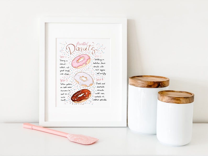May include: A framed illustration of three donuts with pink, white, and chocolate frosting. The illustration is surrounded by colorful sprinkles and includes instructions for making donuts. The text reads "Frosted Donuts" and includes four steps for making donuts.