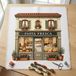 Peut inclure: Un projet de broderie au point de croix sur tissu blanc représentant une devanture de magasin avec le texte PASTA FRESCA. Le motif montre un bâtiment à deux étages avec un toit en tuiles rouges, des volets verts et des jardinières.