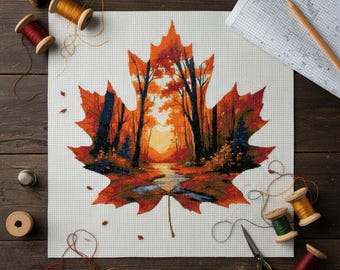 May include: A cross-stitch project depicting a fall landscape within a maple leaf shape. The leaf is in shades of orange and red, with a forest scene inside. Sewing supplies, including thread spools and thimbles, surround the project on a wooden surface.