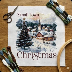 Könnte beinhalten: Kreuzstich-Stickerei einer verschneiten Weihnachtsdorf-Szene mit einem geschmückten Baum und einer Kirche. Die Worte "Small Town Christmas" sind in Braun gestickt. Stickgarn, Schere und ein Stickrahmen umgeben die Leinwand.