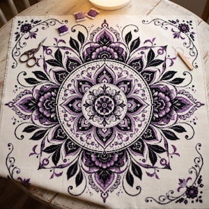 May include: A square piece of off-white fabric featuring a detailed purple and black mandala cross-stitch pattern. The design includes symmetrical floral and geometric motifs. Metal embroidery scissors and a wooden needle tool rest on the fabric.