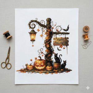 Op de afbeelding: Kruissteekontwerp met een Halloween-scène. Een lantaarnpaal is versierd met pompoenen, herfstbladeren en een bord met de tekst "Happy Halloween". Twee zwarte katten zitten aan de basis. Een verlichte lantaarn hangt aan de paal.