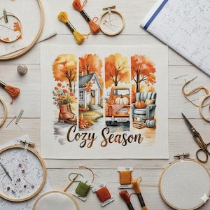 Peut inclure: Un projet de point de croix sur le thème de l'automne, représentant une scène chaleureuse avec une maison, un camion et un fauteuil. Les mots "Cozy Season" sont affichés. Des cerceaux à broder, du fil et des aiguilles entourent le projet.