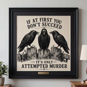 May include: A framed cross-stitch artwork featuring three black crows perched on a wooden fence. The text reads IF AT FIRST YOU DON'T SUCCEED IT'S ONLY ATTEMPTED MURDER. The piece is set in a black frame with a small gold plaque labeled Attempted Murder.