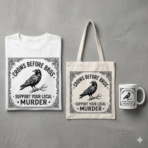 Może przedstawiać: Biała koszulka, beżowa torba i biały kubek z czarną ilustracją kruka i napisem "Crows Before Bros. Support Your Local Murder." Kruk siedzi na gałęzi w ozdobnej ramie.