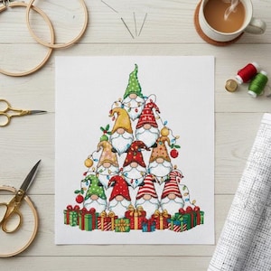 May include: A cross-stitch pattern featuring a Christmas tree made of gnomes with various colorful hats and beards. The gnomes are surrounded by wrapped gifts. Embroidery hoops, scissors, and a cup of coffee are in the background.