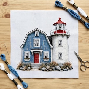 Peut inclure: Un projet de broderie au point de croix sur toile Aida blanche représentant une maison bleue avec une porte rouge accolée à un phare blanc au toit rouge. Le motif inclut des rochers, des fenêtres et est entouré de fils à broder bleus et blancs.