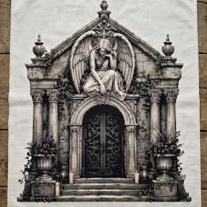 May include: A rectangular white fabric piece featuring a detailed cross-stitch embroidery of a stone mausoleum. The design depicts a winged angel figure sitting above a dark arched doorway, flanked by stone columns, planters, and lit candles.