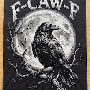 May include: Black and white cross-stitch of a raven perched on a branch in front of a full moon. The text "F-CAW-F" is arched above the raven. The artwork is on a black background.