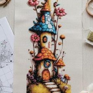 May include: A colorful cross-stitch of whimsical mushroom houses with orange, blue, and yellow roofs, surrounded by pink flowers. The artwork is on a cream-colored fabric, with embroidery hoops, thread, and scissors nearby.