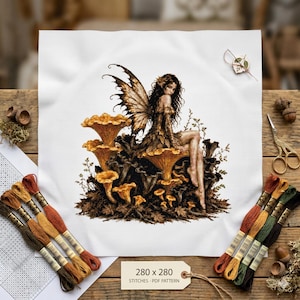 May include: A cross-stitch pattern on white fabric featuring a fairy with brown wings sitting on golden mushrooms. The design includes brown, orange, and green embroidery floss, a needle, and a tag labeled 280 x 280 STITCHES - PDF PATTERN.