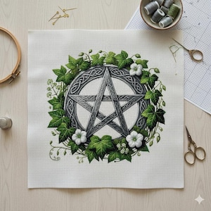 May include: Cross-stitch design featuring a silver pentagram encircled by a Celtic knot design and a wreath of green ivy and white flowers. The embroidery is on white fabric, with sewing supplies in the background.