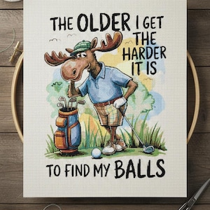May include: Cross-stitch art featuring a cartoon moose in golf attire, leaning on a golf bag. The text reads, "THE OLDER I GET THE HARDER IT IS TO FIND MY BALLS." The moose wears a green hat, blue shirt, and khaki shorts.