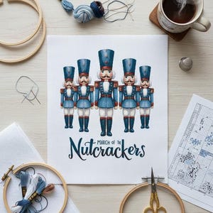 Pode incluir: Um projeto de ponto cruz com cinco quebra-nozes de brinquedo em uniformes azuis e vermelhos. As palavras "March of the Nutcrackers" estão abaixo das figuras. Bastidores de bordado, linha e uma xícara de café também são visíveis.