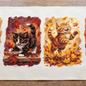 Puede incluir: Un paño de cocina rectangular de color blanco con cuatro paneles impresos de gatitos en entornos otoñales. Las escenas incluyen un gatito en una taza, un gatito caminando entre hojas rojas, un gatito jugando en hojas amarillas y un gatito durmiendo entre calabazas.
