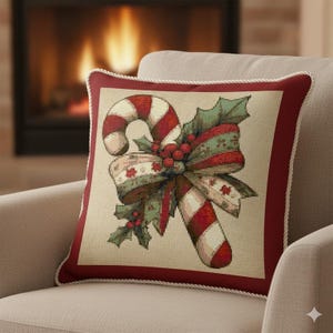 May include: Square decorative pillow with a Christmas candy cane design. The pillow features a red and white candy cane, a green and red bow, and holly leaves. The pillow has a red border with a white rope trim.