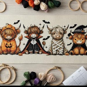 May include: A cross-stitch design featuring four Highland cows dressed in Halloween costumes. One cow wears an orange pumpkin hoodie, another a vampire cape, a third is wrapped in bandages, and the last wears a witch hat. Bats and stars are also stitched.