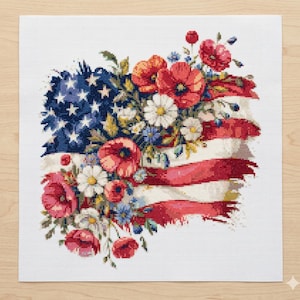 Może przedstawiać: Wzór haftu krzyżykowego przedstawiający amerykańską flagę ozdobioną kwiatami. Gwiazdy i paski flagi są częściowo zasłonięte przez czerwone maki, białe stokrotki i niebieskie dzikie kwiaty, tworząc patriotyczną i artystyczną kompozycję.